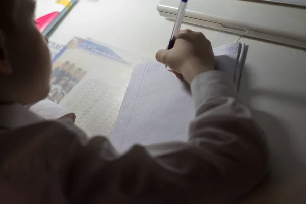 Niño con lápiz escribiendo palabras en inglés a mano en papel blanco tradicional de bloc de notas . —  Fotos de Stock