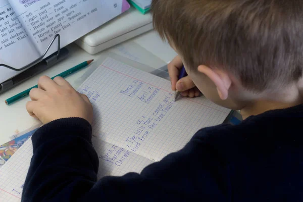 Chlapec s tužkou psát anglická slova ručně na tradiční bílý Poznámkový blok papíru. — Stock fotografie