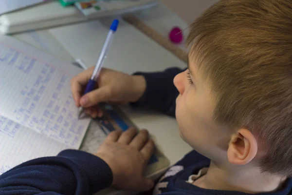 Niño con lápiz escribiendo palabras en inglés a mano en papel blanco tradicional de bloc de notas . — Foto de Stock