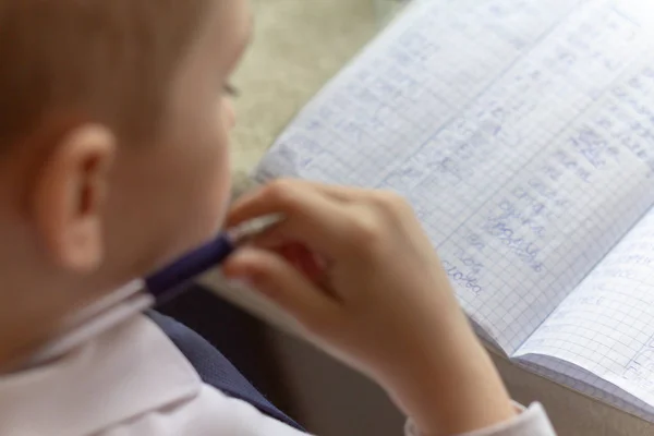 Éducation à domicile. Travail à domicile après l'école. Garçon avec stylo écrire des mots anglais à la main sur papier bloc-notes blanc traditionnel . — Photo