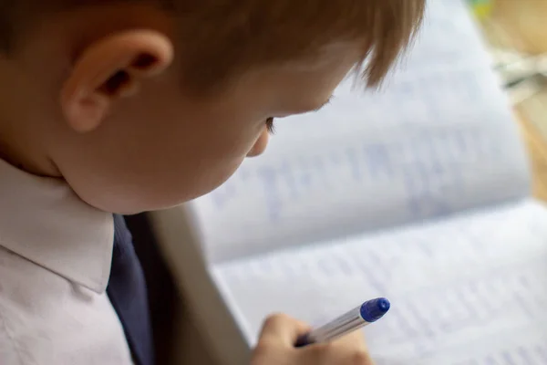 Bildung zu Hause. Heimarbeit nach der Schule. Junge mit Stift schreibt englische Wörter von Hand auf traditionelles weißes Notizblock-Papier. — Stockfoto