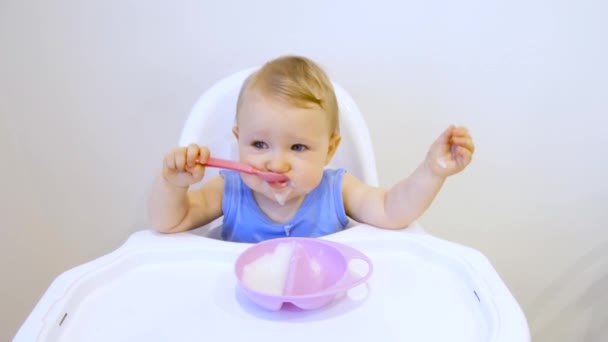 Uma criança pela primeira vez em sua vida come mingau de cereal. A criança come pela primeira vez sozinha. — Vídeo de Stock