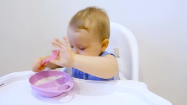 Uma criança pela primeira vez em sua vida come mingau de cereal. A criança come pela primeira vez sozinha. — Vídeo de Stock