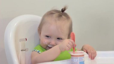 Kız ilk kez kendi başına yiyor, şımartıyor ve gülüyor. Çocuk plastik kaşıkla süzme peynir yiyor. İlk kez. Çocuk ilk kez kendi başına yiyor.