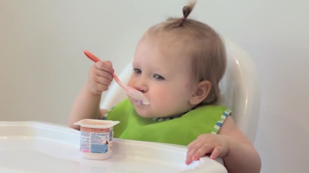 Kız ilk kez kendi başına yiyor, şımartıyor ve gülüyor. Çocuk plastik kaşıkla süzme peynir yiyor. İlk kez. Çocuk ilk kez kendi başına yiyor. — Stok video