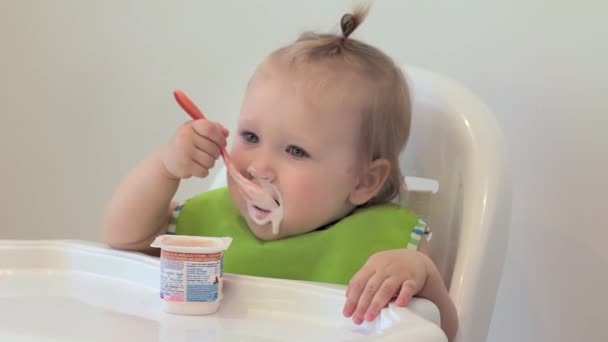 女の子は一人で初めて食べる,ふけると笑い.子供はプラスチックスプーンでカッテージチーズを食べます。初めてだよ。子供は１人で初めて食べる — ストック動画