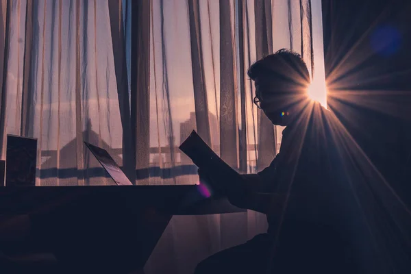 Modern bir odada sabah güneşinin aydınlattığı pencereye karşı kitap okuyan bir adamın silueti biraz göz kamaştırıcı..