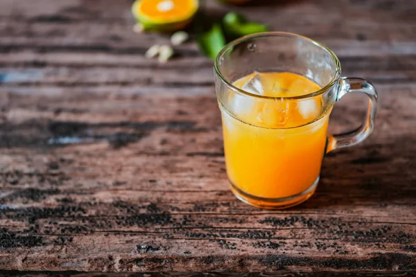 Bir bardak portakal suyu eski ahşap bir masada, taze yerel portakal dilimleri ve yapraklarıyla tamamlanmış. Endonezya 'da buna 