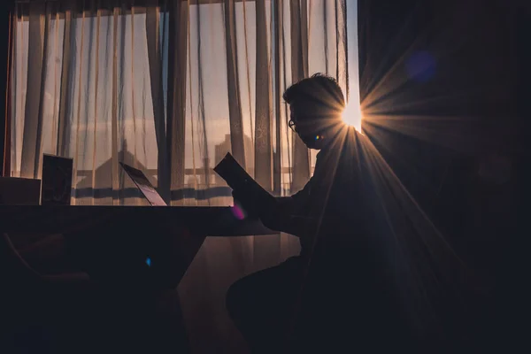 Modern bir odada sabah güneşinin aydınlattığı pencereye karşı kitap okuyan bir adamın silueti biraz göz kamaştırıcı..