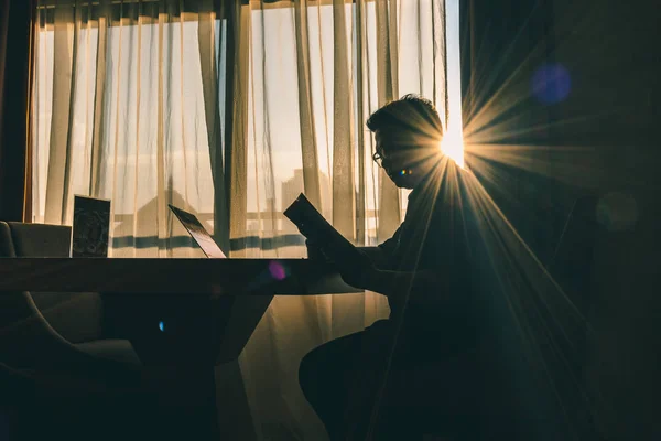 Modern bir odada sabah güneşinin aydınlattığı pencereye karşı kitap okuyan bir adamın silueti biraz göz kamaştırıcı..