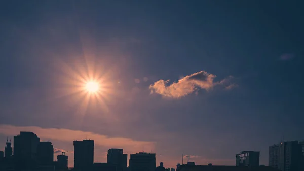 Güneş parlak mavi gökyüzünde bulutların arasında parlıyor.
