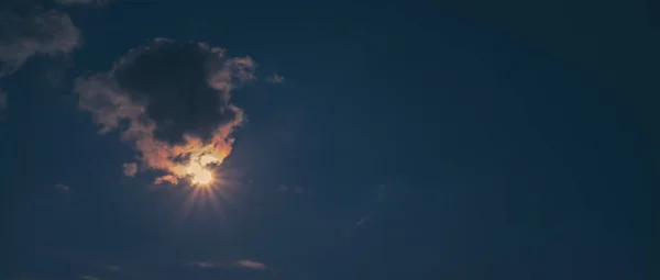 Güneş parlak mavi gökyüzünde bulutların arasında parlıyor.