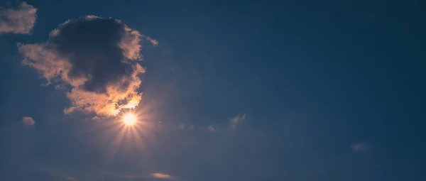 Güneş parlak mavi gökyüzünde bulutların arasında parlıyor.