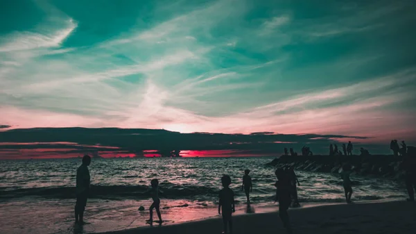 Gün batımında sahilde insan siluetleri.