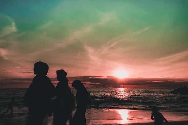 Gün batımında sahilde insan siluetleri.