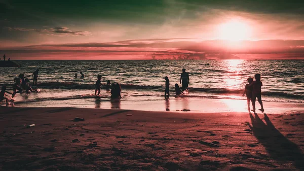 Gün batımında sahilde insan siluetleri.