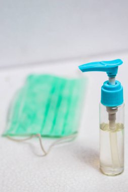 El dezenfektanı şişesi ve ameliyat maskesi dikey olarak beyaz yüzeyde. Virüs hastalıklarında veya covid-19 ve filovirüs gibi salgınlarda kullanılmak üzere genel kişisel koruma ekipmanları.