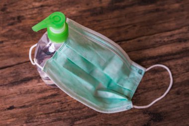 Ahşap masa arkasında el dezenfektanı şişesini örten cerrahi maske. Virüs hastalıklarında veya covid-19 ve filovirüs gibi salgınlarda kullanılmak üzere genel kişisel koruma ekipmanları.