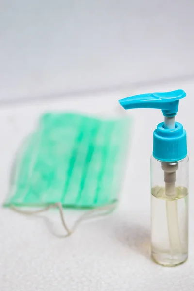 El dezenfektanı şişesi ve ameliyat maskesi dikey olarak beyaz yüzeyde. Virüs hastalıklarında veya covid-19 ve filovirüs gibi salgınlarda kullanılmak üzere genel kişisel koruma ekipmanları.