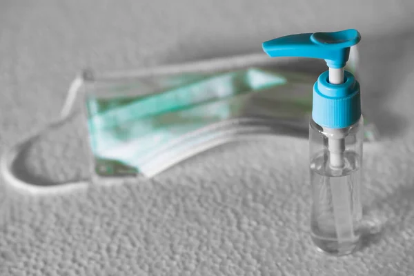 Şeffaf şişede antiseptik sıvı ve beyaz yüzeyde cerrahi maske. Virüs hastalıklarında veya covid-19 ve filovirüs gibi salgınlarda kullanılmak üzere genel kişisel koruma ekipmanları.