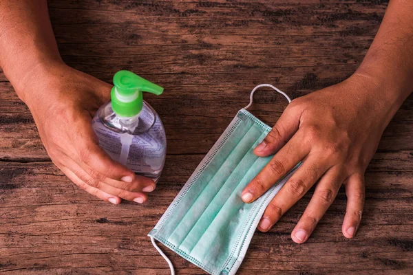 Eller ahşap masada el dezenfektanı şişesi ve tıbbi maske tutsun. Virüs hastalıklarında veya covid-19 ve filovirüs gibi salgınlarda kullanılmak üzere genel kişisel koruma ekipmanları.