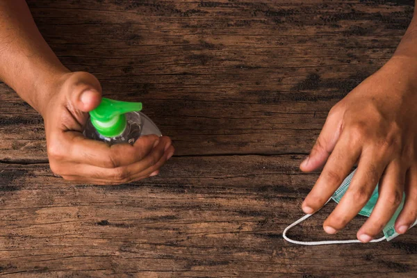 Eller ahşap masada el dezenfektanı şişesi ve cerrahi maske tutuyor. Virüs hastalıklarında veya covid-19 ve filovirüs gibi salgınlarda kullanılmak üzere genel kişisel koruma ekipmanları.