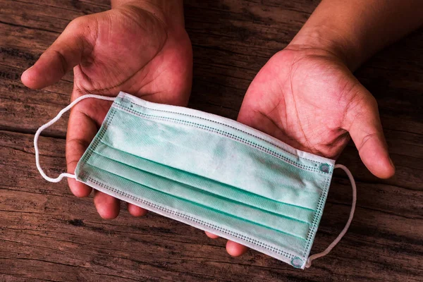Ahşap masada cerrahi maske gösteren bir adamın elleri. Virüs salgınları sırasında insanları tıbbi maske bağışlamaya davet eden bir resim, covid-19 salgını gibi. .