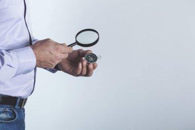 Gri arka planda büyüteçle pusula tutan adam.