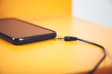 Turuncu arka planda akıllı telefonu olan kulaklık.