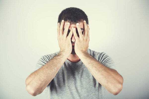 young sad man hand in face on gray background