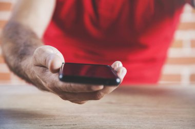 Genç adam elinde siyah akıllı telefon tutuyor.