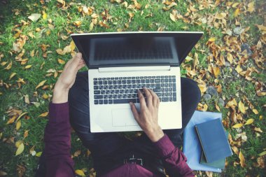 İnsan eli bilgisayarı doğada çimlerde oturuyor.