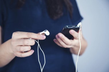 Kadın elinde kulaklıkla akıllı telefonu tutuyor.