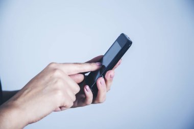 Gri duvar arka planında kadın eli akıllı telefon.
