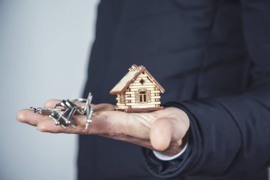 Adam ahşap ev modelini anahtarla tutuyor.