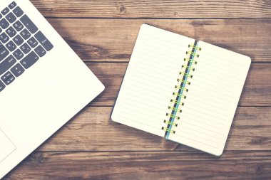 Tahta masa arkaplanındaki bilgisayar klavyesindeki not defteri