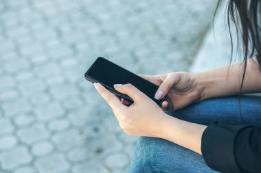 Parkta akıllı telefon kullanan genç bir kadın.