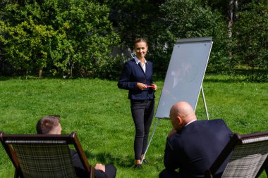 Kadın ayağa kalk ve sandalyedeki erkeklerle konuş.