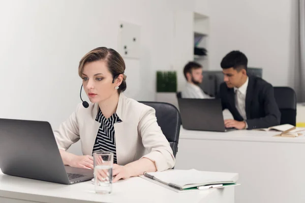 Geschäftsfrau mit Mikroarbeiten, Kollegen sitzen an einem Tisch im Hintergrund — Stockfoto