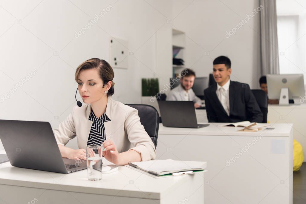 Woman with a micro work on a laptop and her collegues look at her