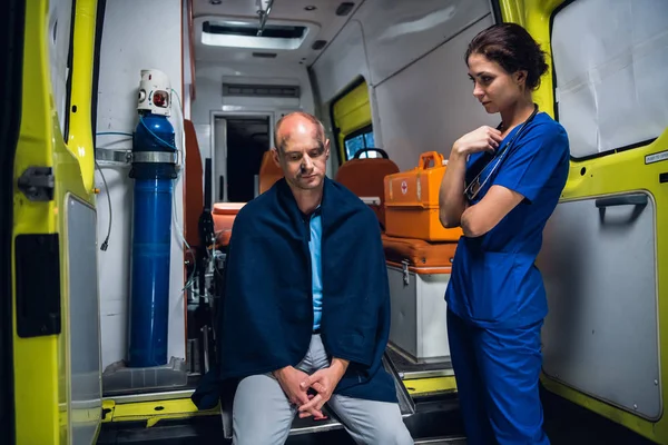 Enfermera parada al lado de un hombre que se sienta en el coche de la ambulancia — Foto de Stock