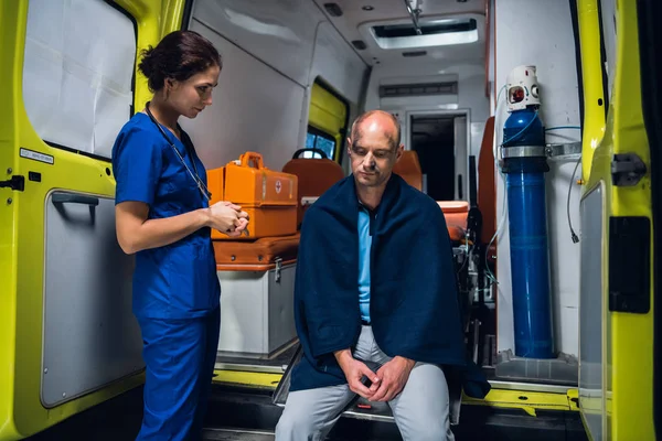 Enfermera de uniforme mira al hombre que se sienta en el coche de la ambulancia — Foto de Stock