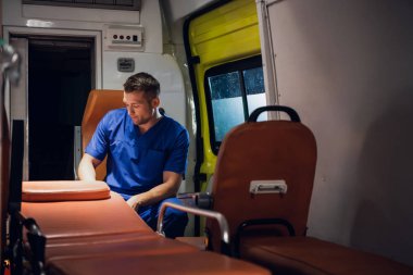 Üniformalı sağlık görevlisi ambulans vagonunda oturur ve bir yere bakar.