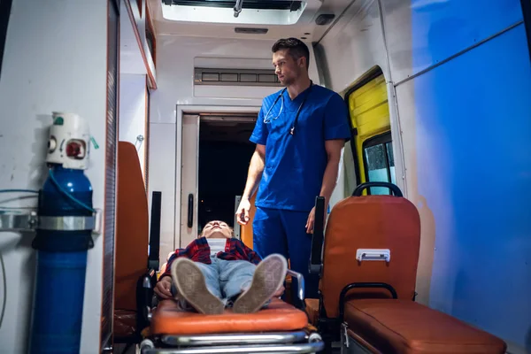 Corpsman se tient à côté d'une femme insensée allongée sur une civière dans la voiture d'ambulance — Photo