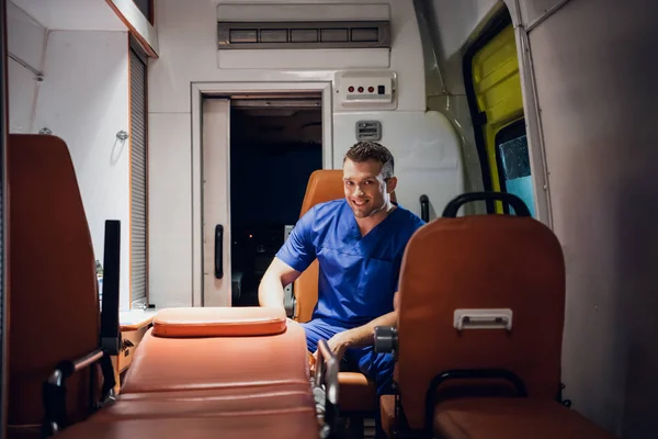 El forense feliz en uniforme se sienta en el coche de la ambulancia y sonríe —  Fotos de Stock