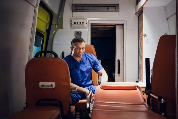 Человек в медицинской форме сидит в машине скорой помощи и улыбается. — стоковое фото