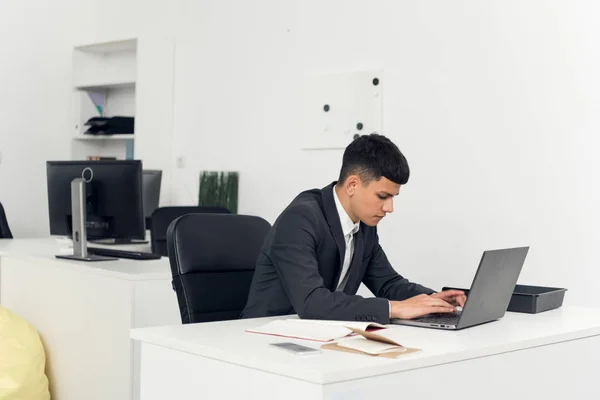 Młody mężczyzna w garniturze siedzi przy stole i pracuje z laptopem — Zdjęcie stockowe