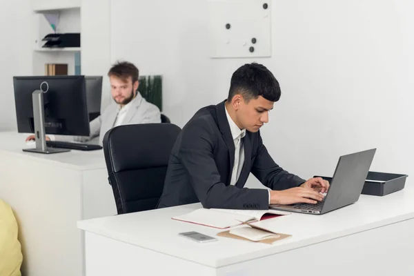 Mężczyźni pracują w biurze, facet w garniturze nagrywa na laptopie. — Zdjęcie stockowe