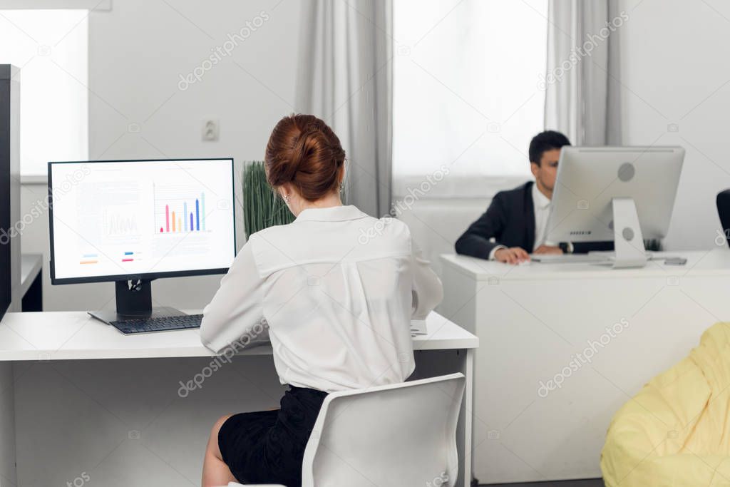 Man and woman in suits sit at tables and work with laptops