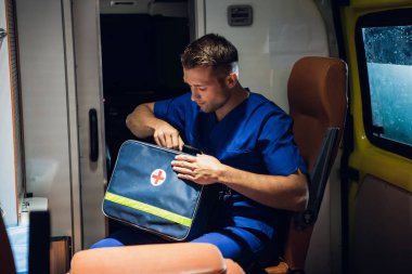 Corpsman in uniform sits in the ambulance car and packs medical bag